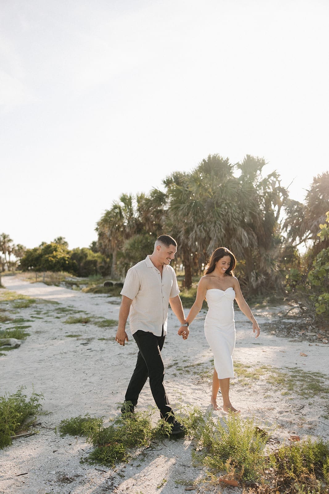 authentic wedding photo of a bride and groom walking hand-in-hand on the beach, smiling