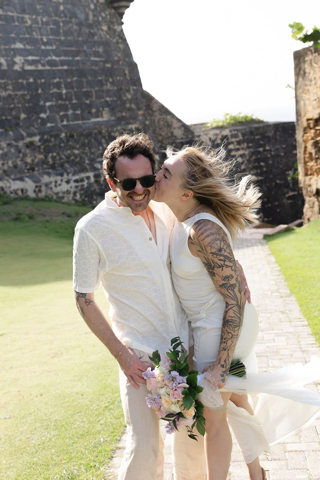 natural wedding photo of a bride kissing her smiling groom on the cheek