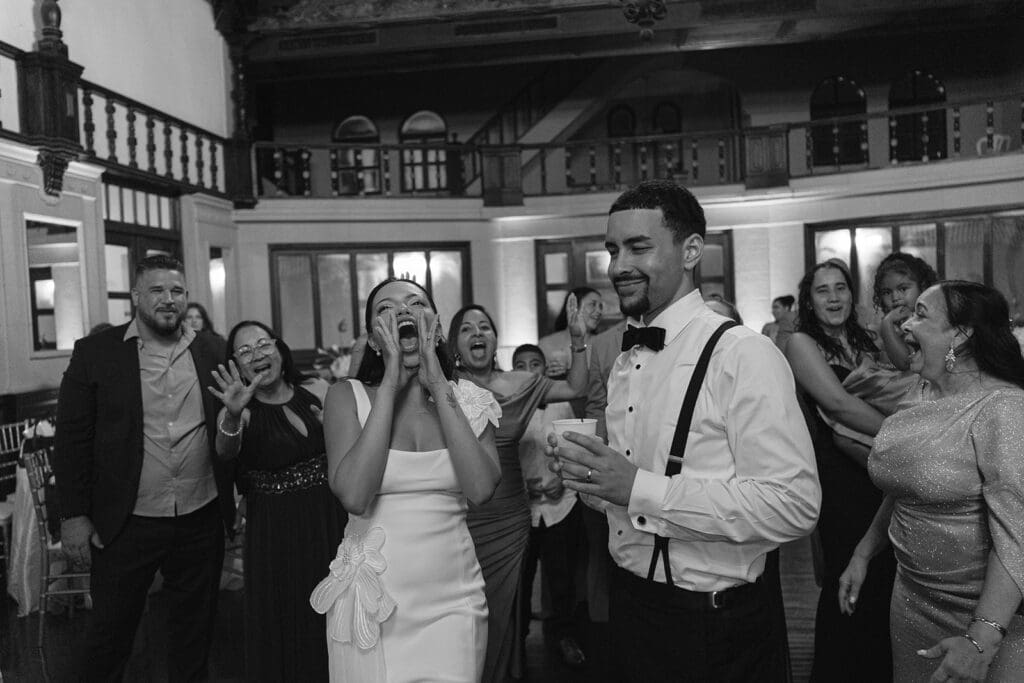 Black-and-white photo of the bride and groom celebrating with cheering wedding guests.