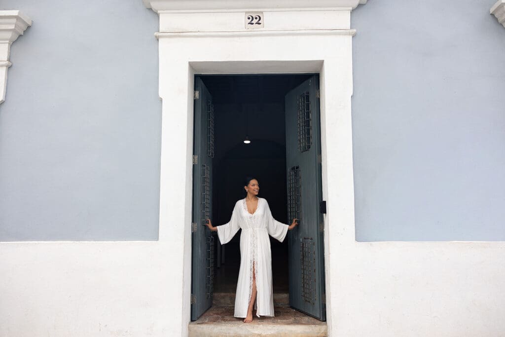 Bride in a white getting-ready robe standing in a blue doorway in Viejo San Juan.