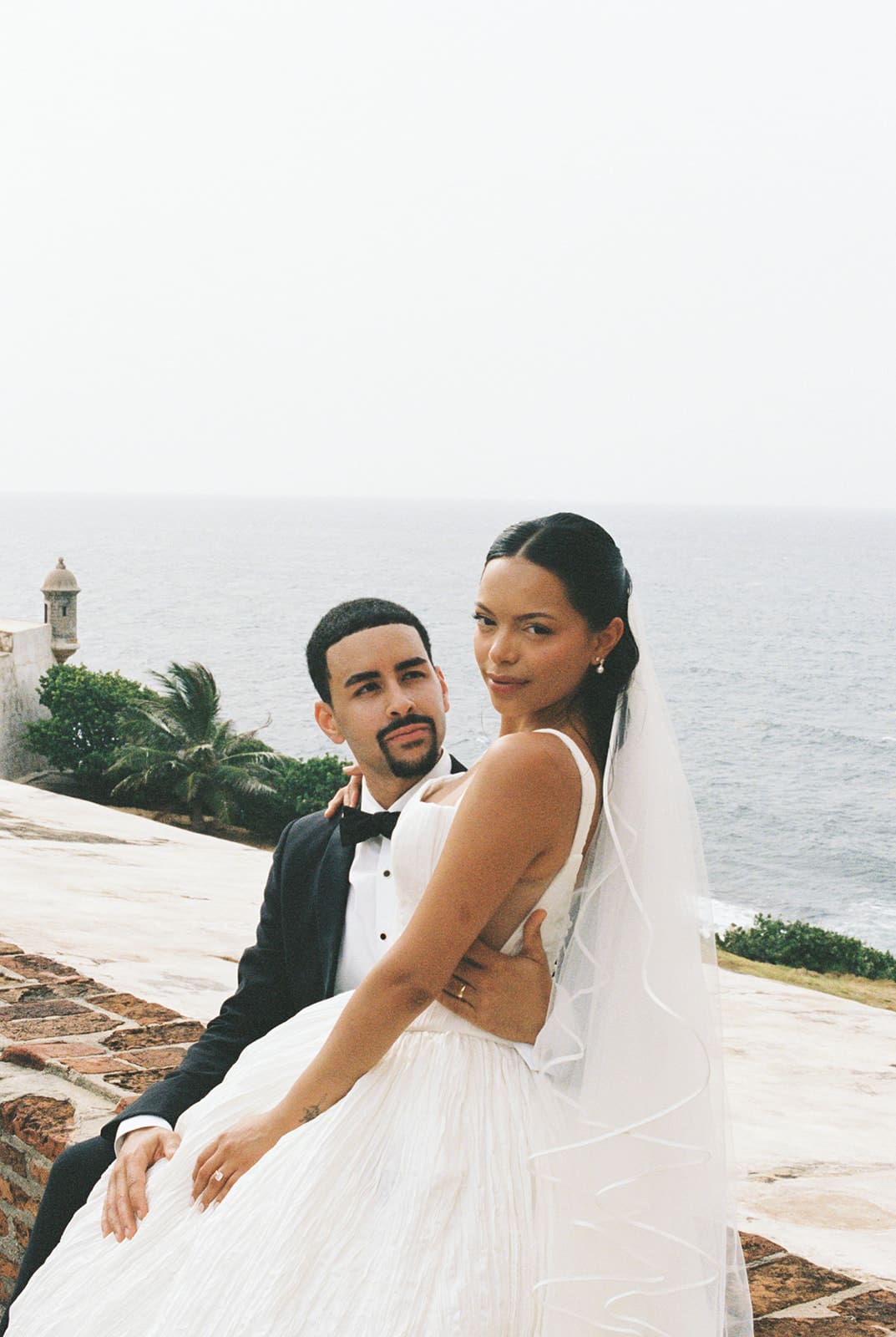 Bride and groom pose together with the ocean behind them at Castillo San Cristóbal in San Juan.