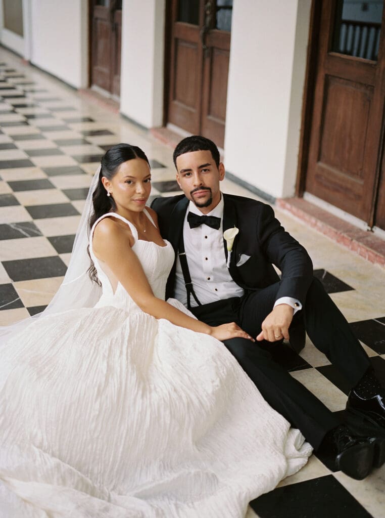 Bride and groom sit together on the checkerboard floor for a wedding portrait at Casa de España.