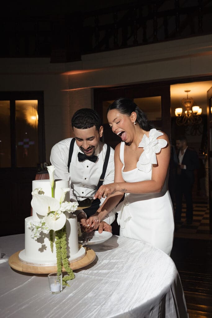Bride and groom laughing together while cutting their wedding cake.