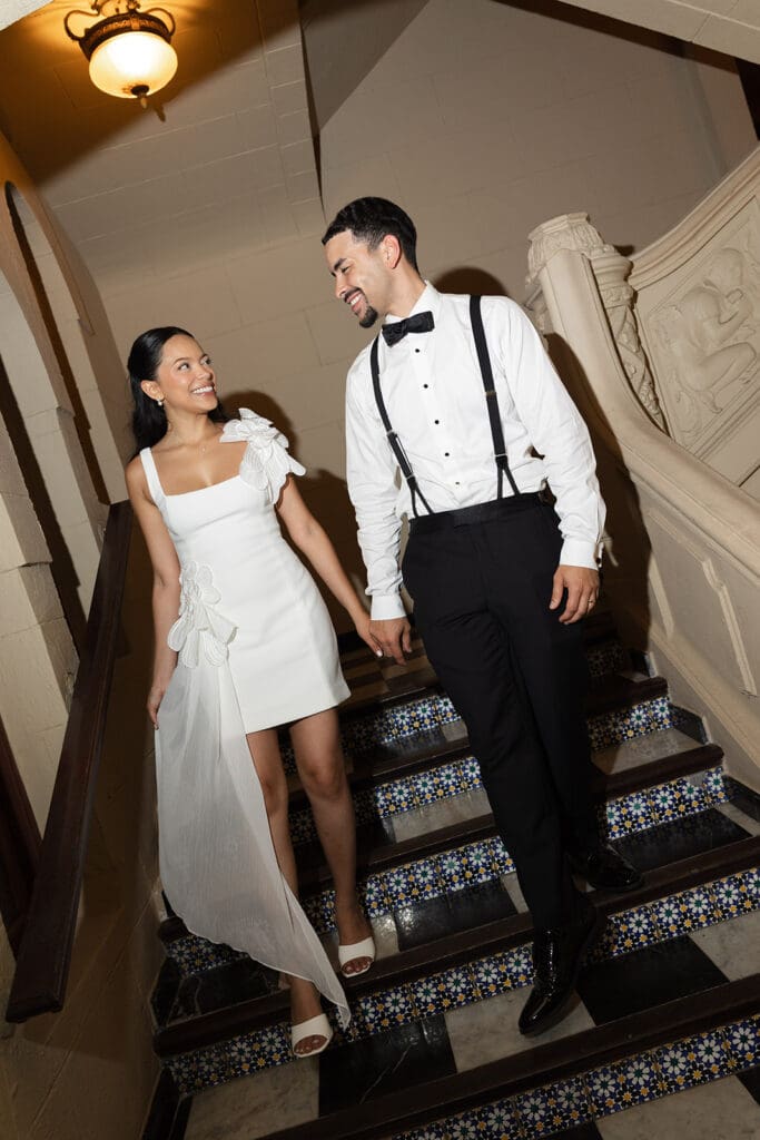 Bride and groom smiling at each other while walking down the tiled staircase at Casa de España.