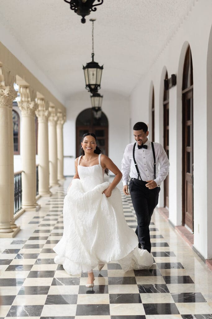Bride and groom laughing as they run through a checkerboard-tiled corridor at Casa de España in Puerto Rico.