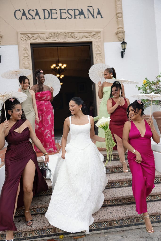 Bride walks down the tiled steps with her wedding party holding white parasols at Casa de España.