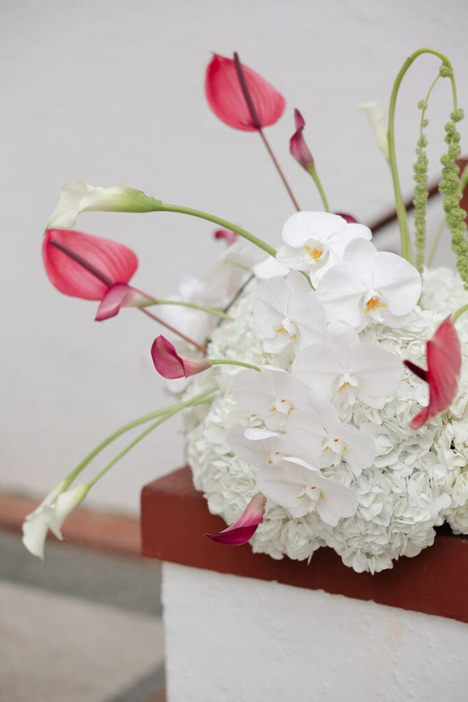 White orchids, hydrangeas, pink anthuriums, and trailing greenery arranged as wedding ceremony flowers.