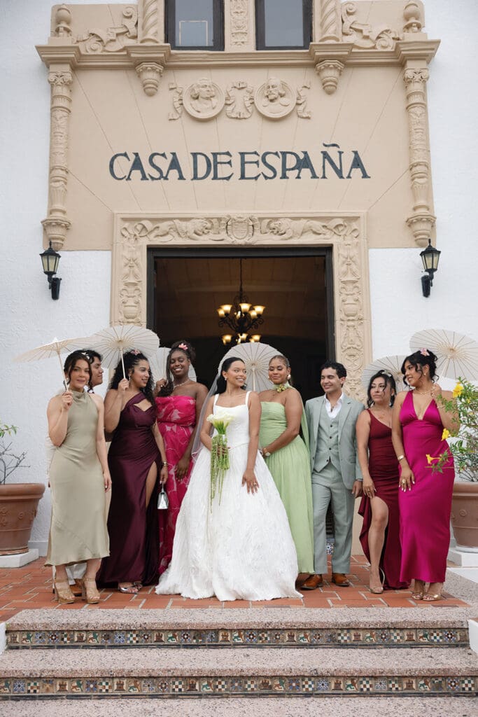 Bride and wedding party pose with white parasols outside the Casa de España entrance.