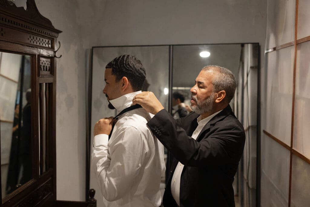 Groom’s father helps adjust his collar while he gets ready for the wedding.