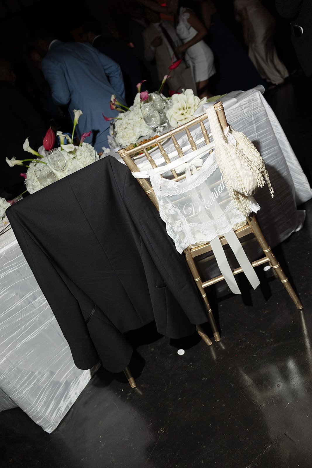 Groom’s black jacket draped over a chair beside the lace “Married” chair decoration at the reception.