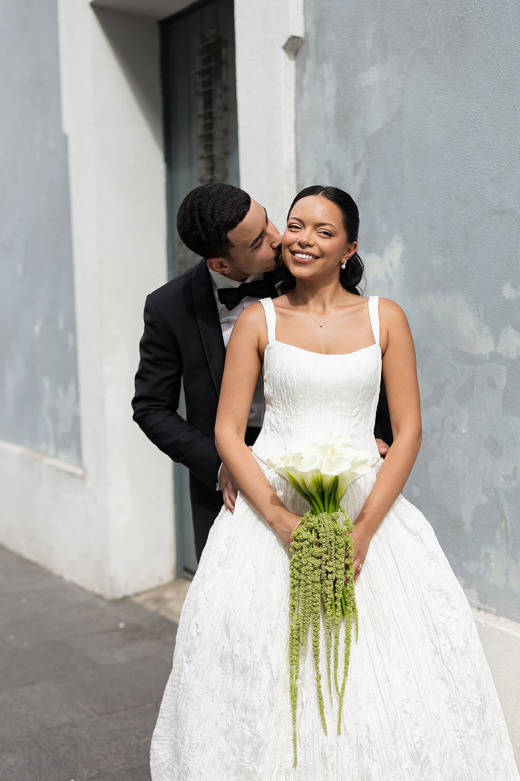 Groom kisses the smiling bride on the cheek as she holds her white calla lily bouquet in Old San Juan.