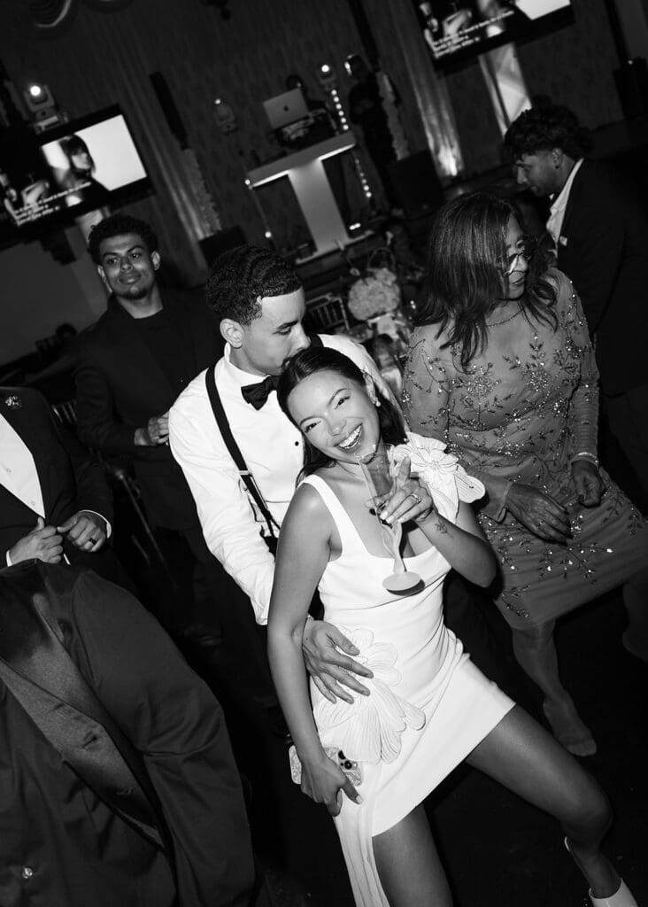 Black-and-white photo of the groom kissing the bride while they dance together at the reception.