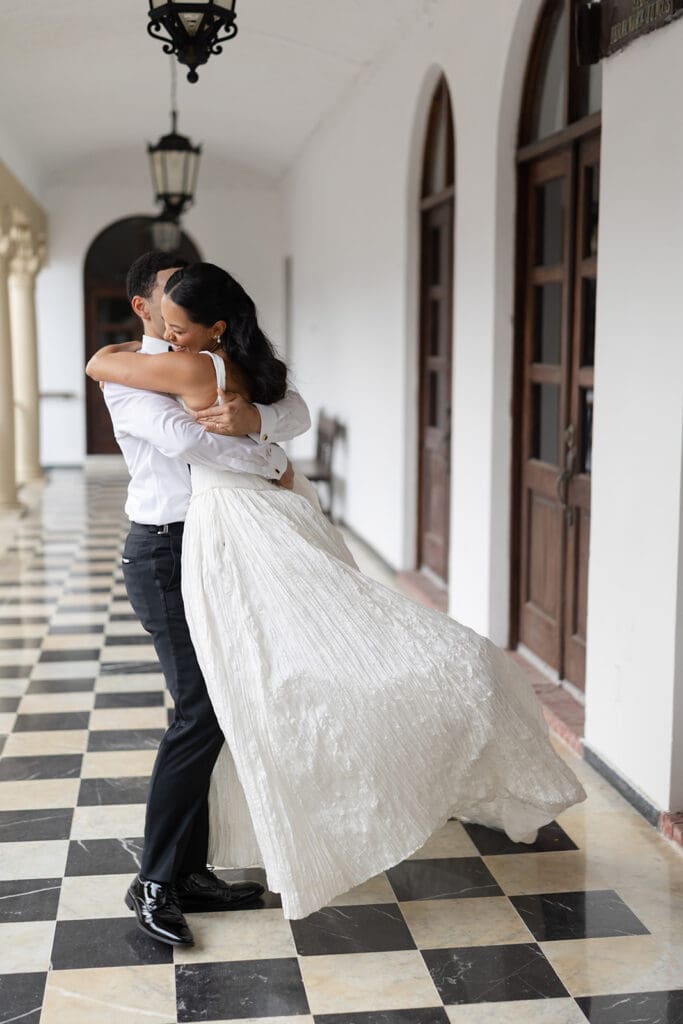 Groom lifts the smiling bride during a playful wedding portrait in a corridor at Casa de España.