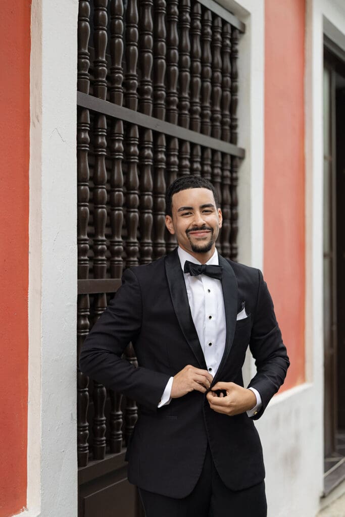 Groom buttoning his black tuxedo jacket for his wedding in Old San Juan.