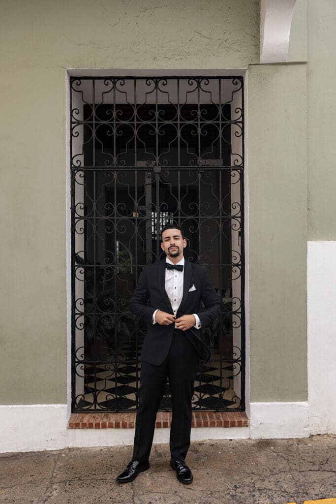 Full-length portrait of the groom in a black tuxedo in front of a wrought-iron gate in Old San Juan.