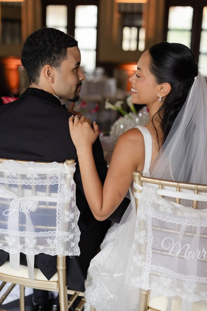 Bride and groom smile at each other while seated together at their Casa de España wedding reception.