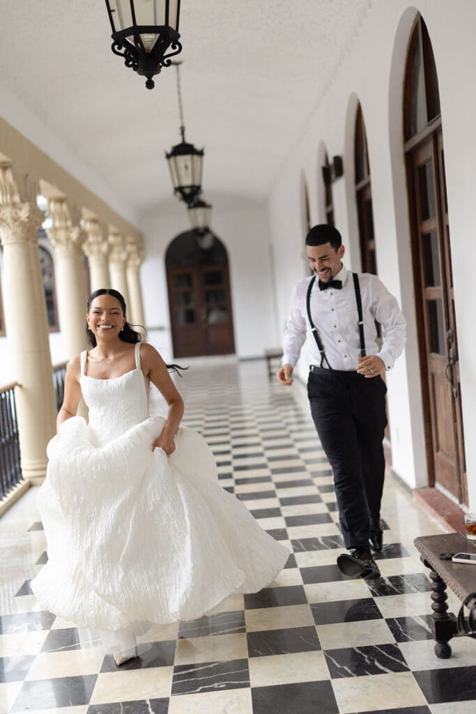 Bride runs laughing with the groom following behind through a tiled corridor at Casa de España.
