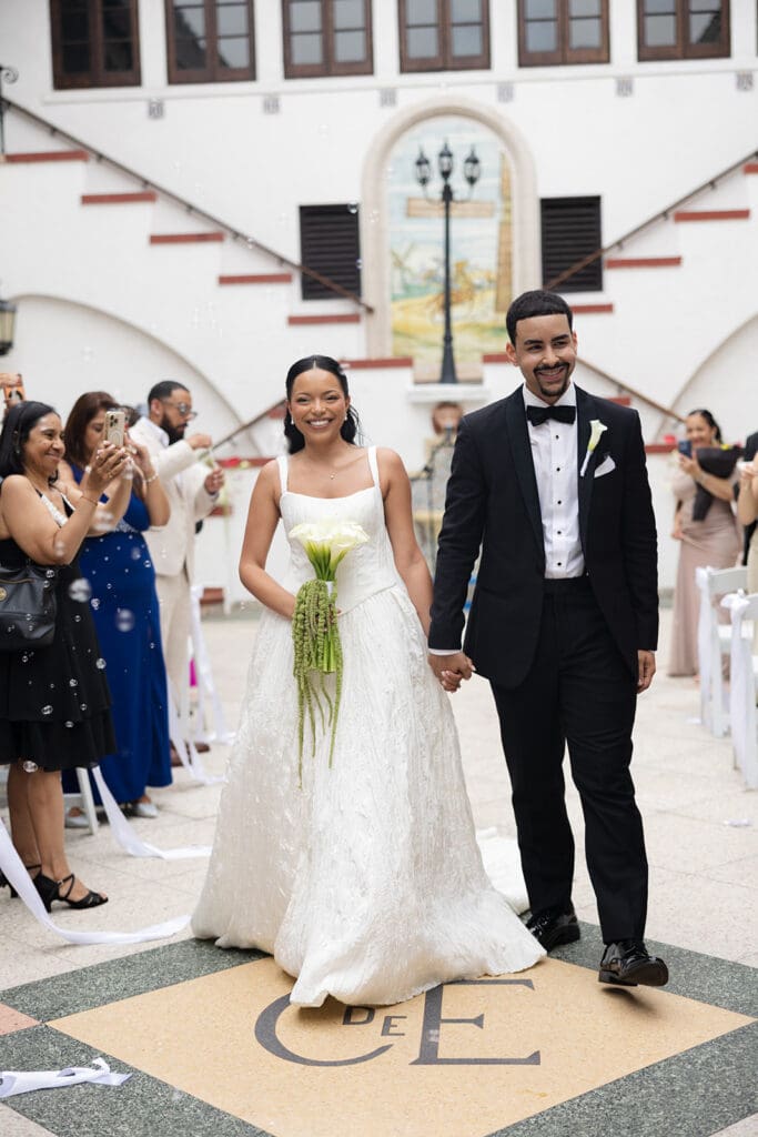 Bride and groom hold hands and smile as they walk down the aisle after their Casa de España wedding ceremony.