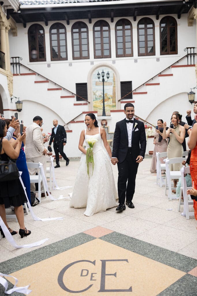 Newlyweds walk through the Casa de España courtyard as wedding guests celebrate around them.