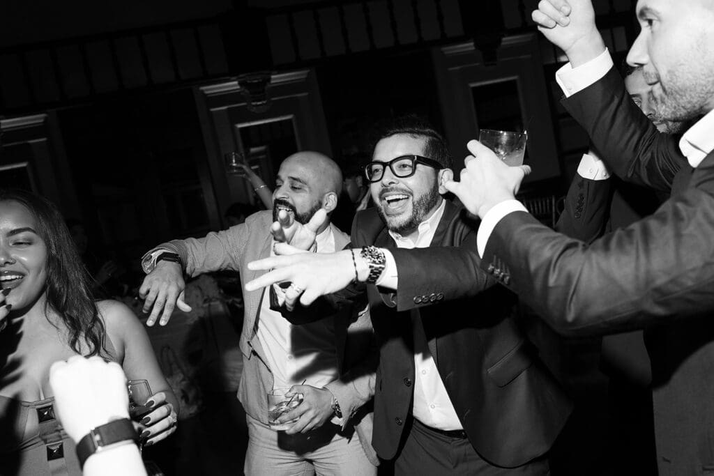Black-and-white photo of wedding guests laughing and dancing together during the reception