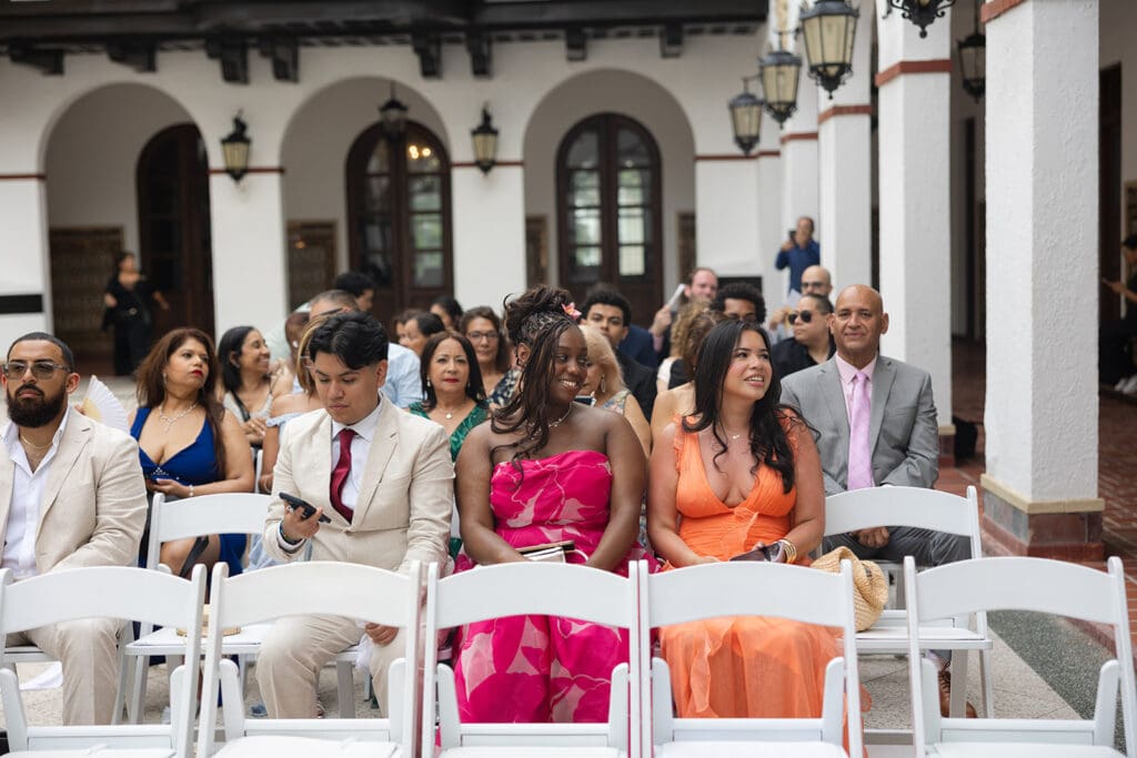 Wedding guests seated on white chairs in the courtyard before the ceremony begins.
