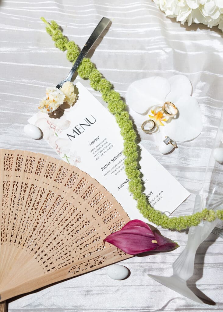 Wedding menu, rings, wooden fan, and floral details arranged on a reception table.