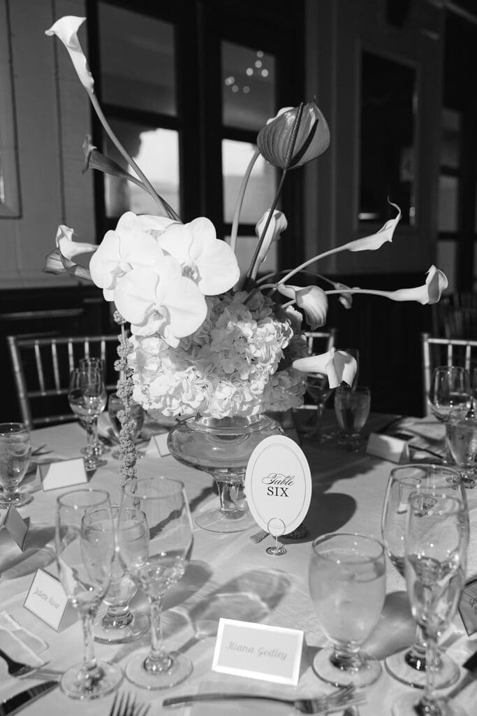 Black-and-white wedding reception table with floral centerpiece and Table Six sign.