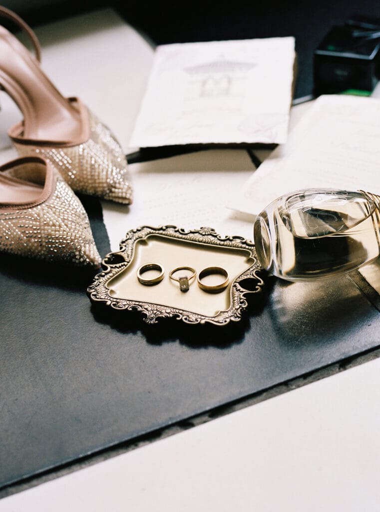 Wedding rings displayed on an ornate tray beside beaded bridal shoes and perfume.