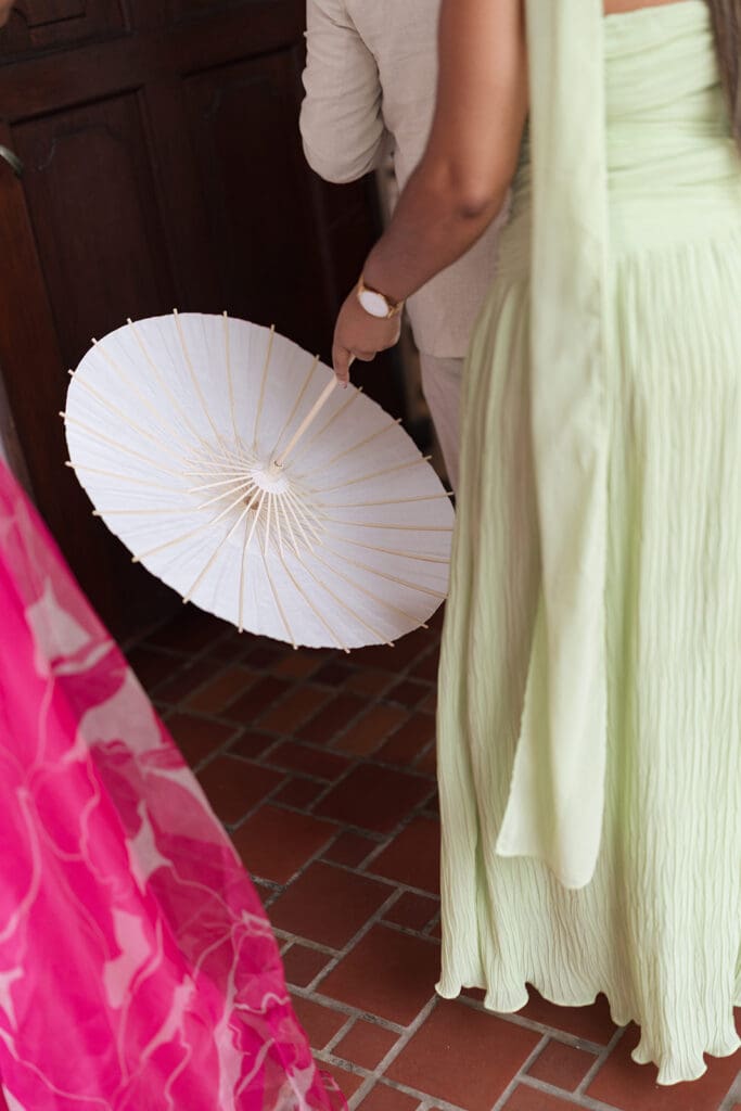 Wedding guest holds a white parasol beside guests dressed in pink and pale green.