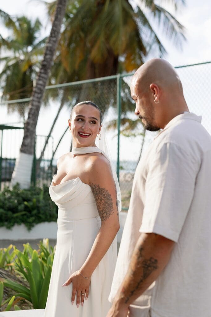 Bride smiling at her partner during their Puerto Rico elopement, with tropical greenery and palm trees in the background.