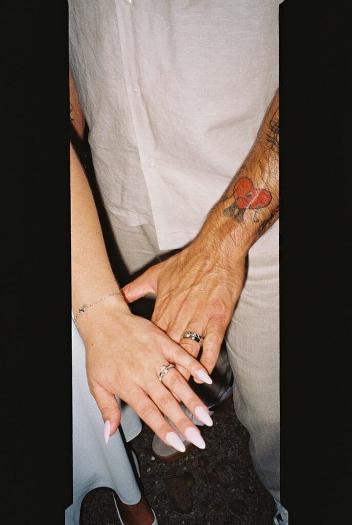 Close-up of the bride and groom's hands showing their wedding rings and the groom's colorful forearm tattoo.