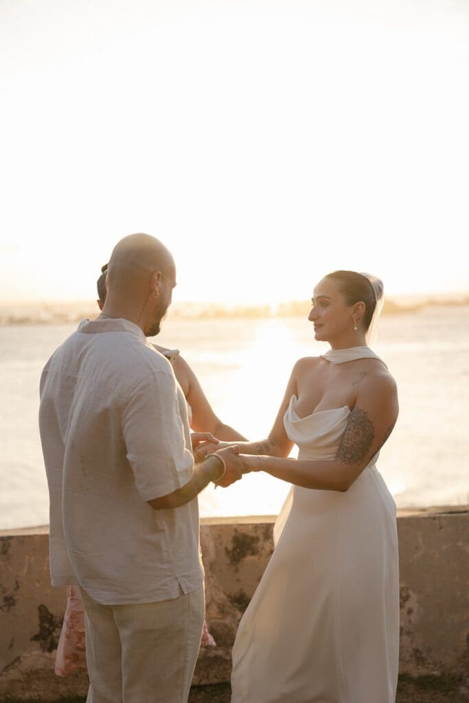 Couple holding hands and exchanging vows during their Puerto Rico elopement at sunset, overlooking the ocean.