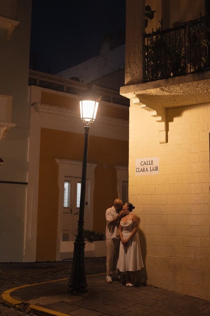 Couple sharing a kiss on a warmly lit street corner in Old San Juan, Puerto Rico, at night.