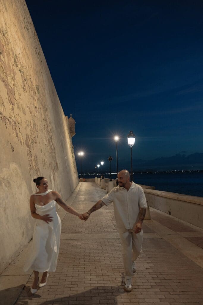 Couple walking hand in hand along the historic fortress walls in Old San Juan during their Puerto Rico elopement at dusk.
