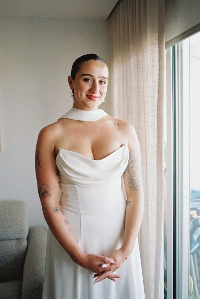 Bride smiling beside a window in a white halter neck wedding dress during her elopement preparations in Puerto Rico.
