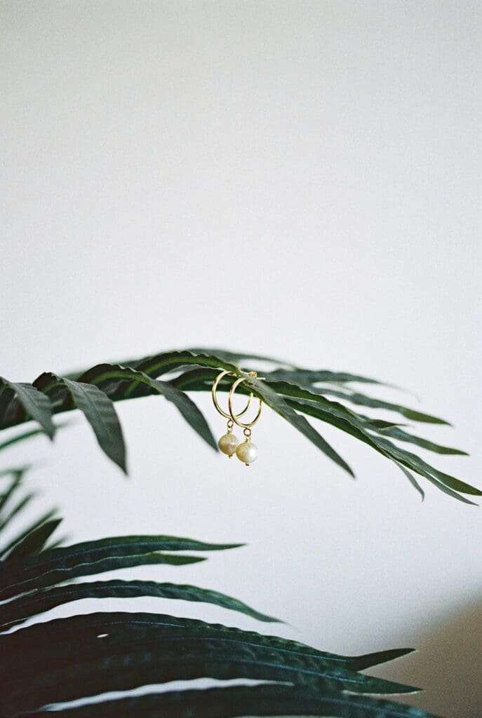 Gold hoop earrings with dangling pearls displayed on tropical green leaves as bridal accessories for a Puerto Rico elopement.