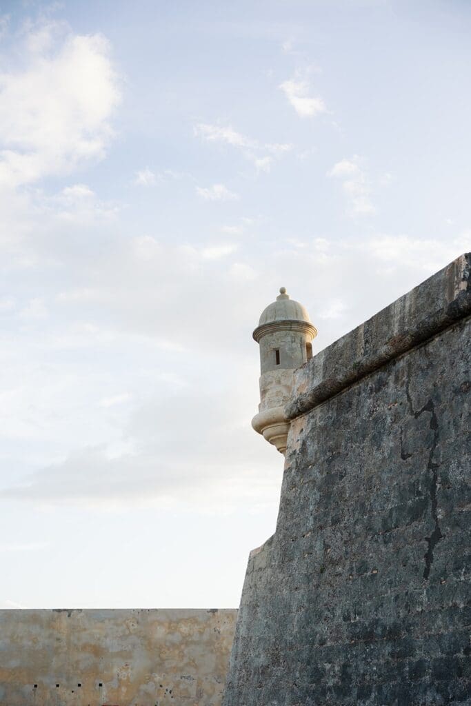 Historic stone fortress wall and watchtower in Old San Juan, Puerto Rico, beneath a partly cloudy sky.