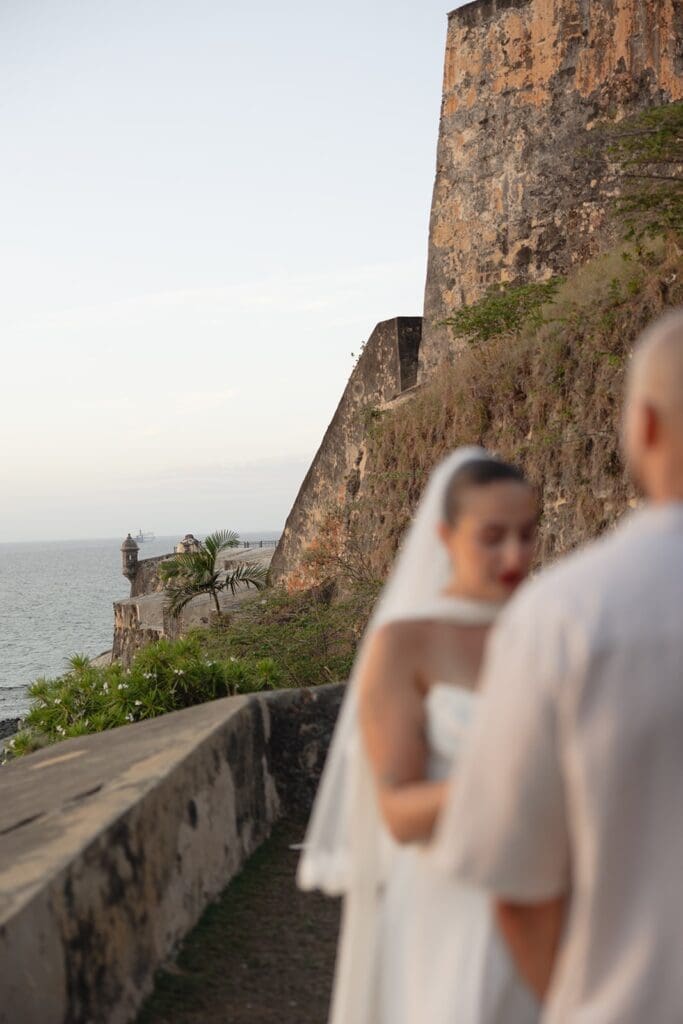 Historic stone fortress walls overlooking the ocean in Old San Juan, with an eloping couple in the foreground.