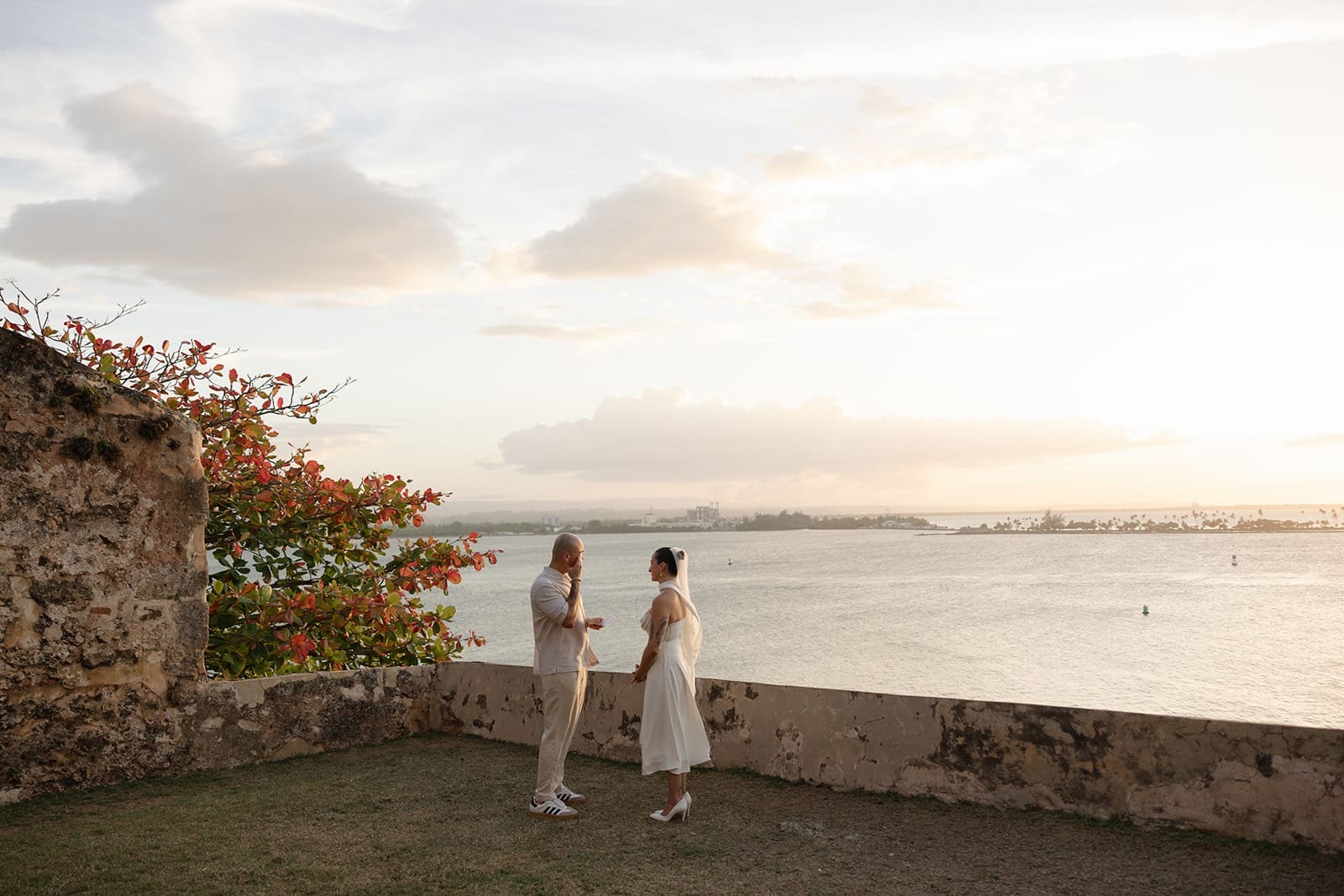 Couple exchanging personal vows during their Puerto Rico elopement at a historic coastal fort overlooking the ocean at sunset.